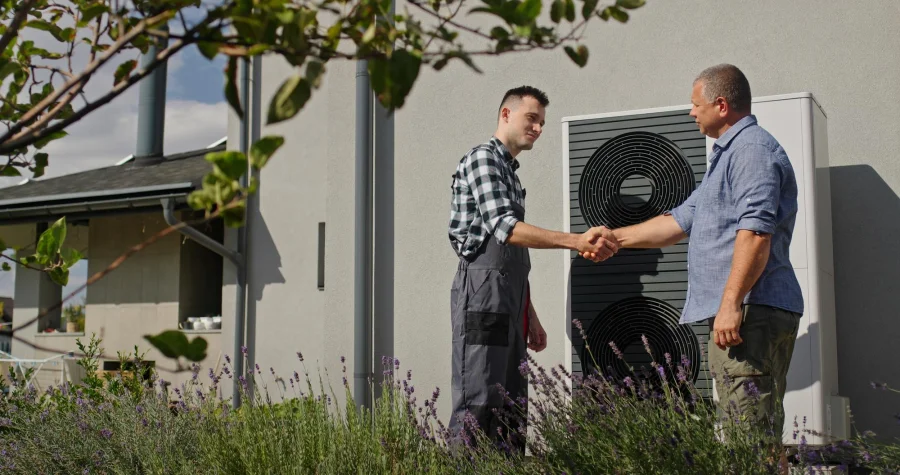 Homeowner greeting an HVAC technician beside an outdoor heating unit